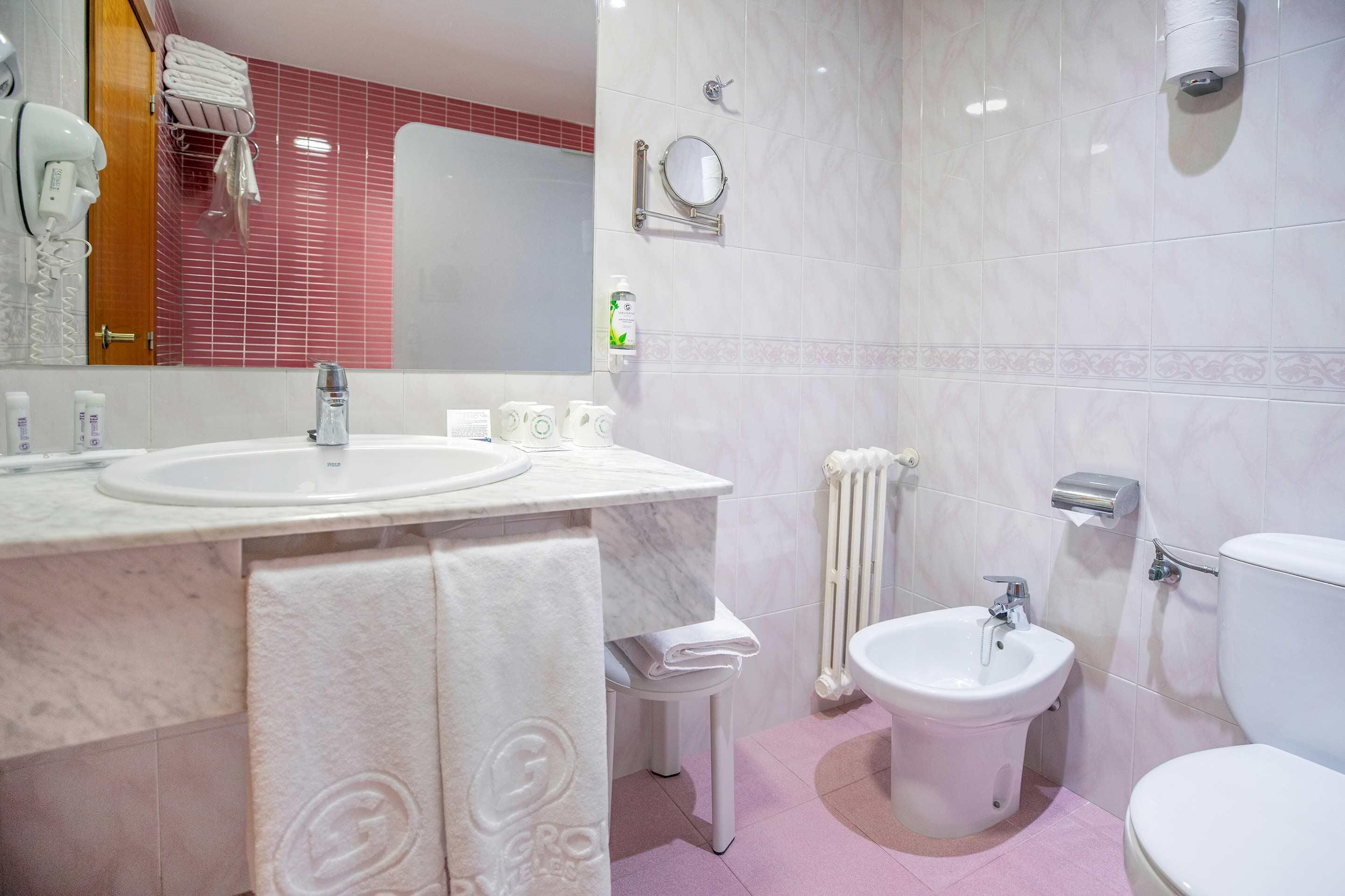 Un baño con dos lavamanos, un bidé, un inodoro, un espejo y un perchero para toallas.