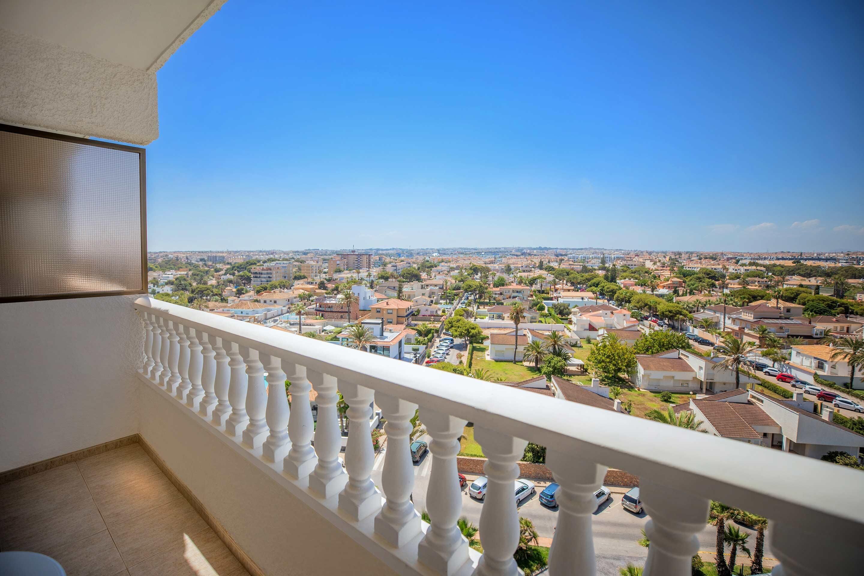 A balcony with a white balustrade overlooking a residential area with houses and parked cars.