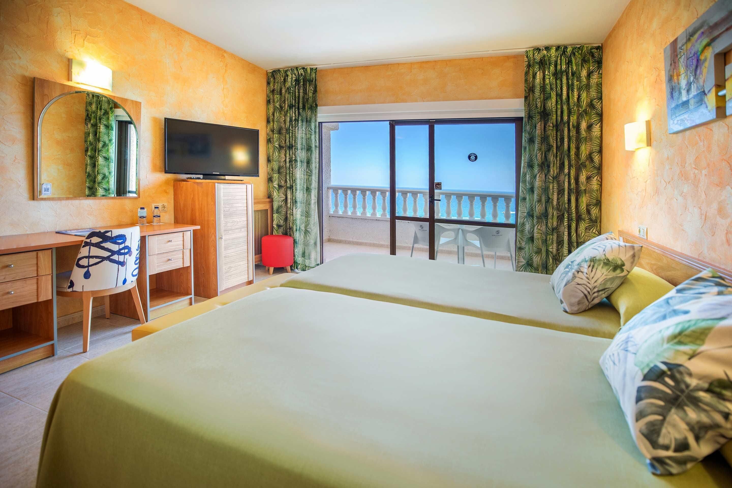 Habitación de hotel con cama, escritorio, televisión y balcón con vistas.