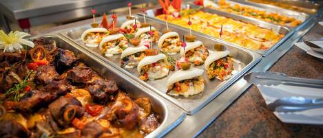 A buffet with various dishes including meat, vegetables, and bread rolls.