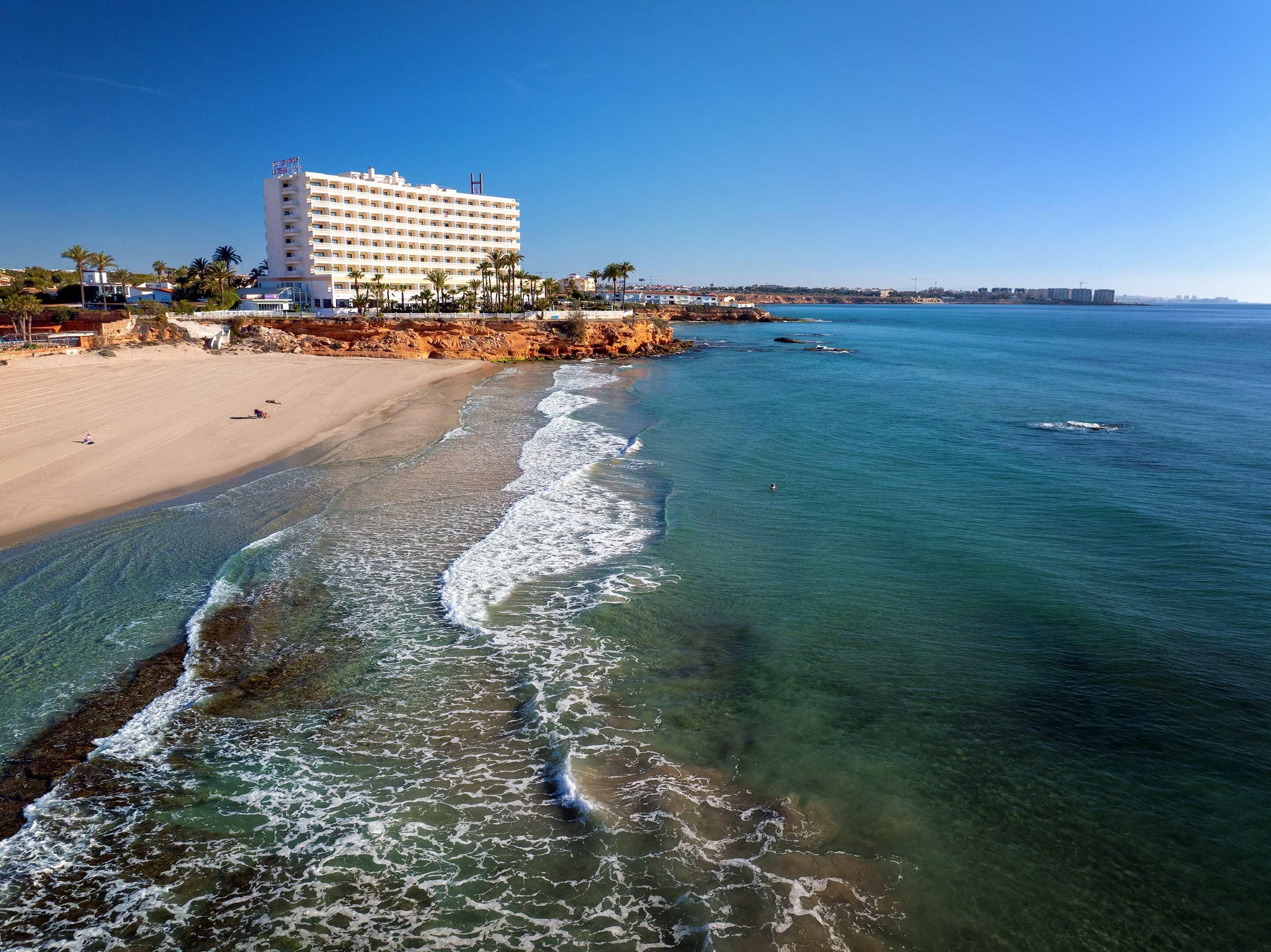 Un hotel frente al mar con vista a la playa, arena dorada y aguas cristalinas.