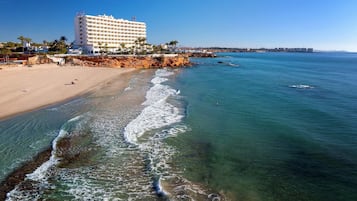 Un hotel frente al mar con vista a la playa, arena dorada y aguas cristalinas.