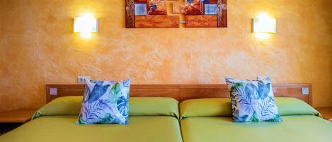 Una cama doble con ropa de cama verde y dos almohadas decorativas, un cabecero de madera y dos lámparas fijadas a la pared.
