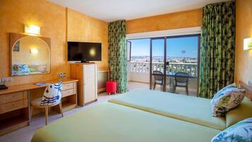 A hotel room with a bed, desk, chair, TV, and balcony with curtains.