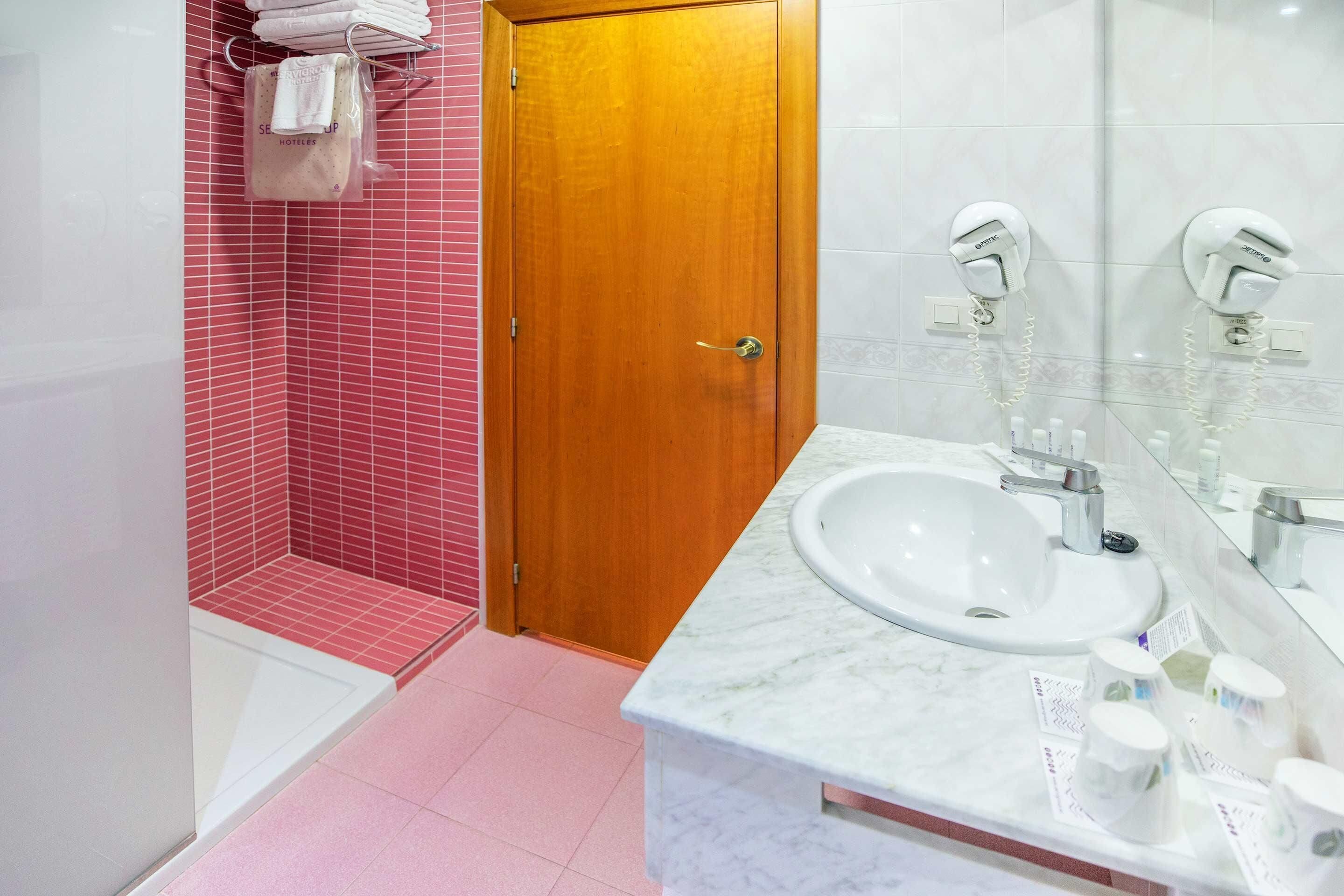 A bathroom with a wooden door, a sink with a mirror, and a shower area with pink tiles.