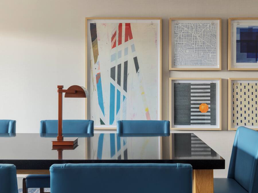 Una sala conferenze con un tavolo in vetro, sedie blu e quadri appesi al muro.