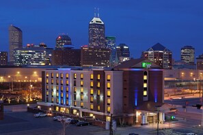 Un hôtel reconnaissable à son grand panneau « Holiday Inn Express », entouré d’un parking et surplombant la silhouette de la ville au crépuscule.