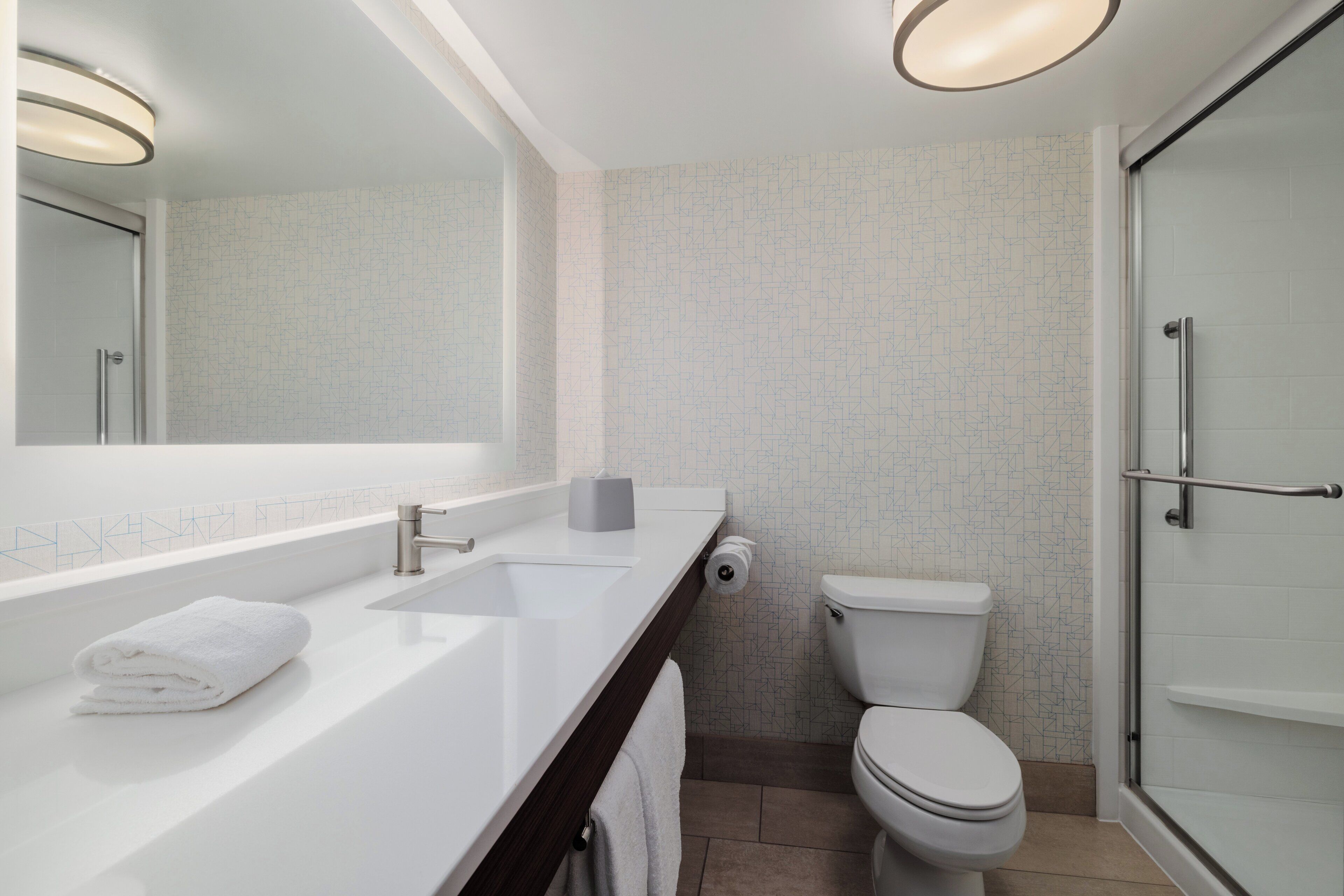 A modern bathroom with a white sink, mirror, toilet, and glass shower enclosure.
