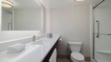 A modern bathroom with a white sink, mirror, toilet, and glass shower enclosure.