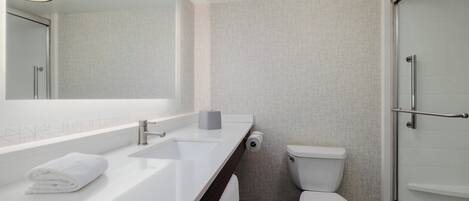A modern bathroom with a white sink, mirror, toilet, and glass shower enclosure.