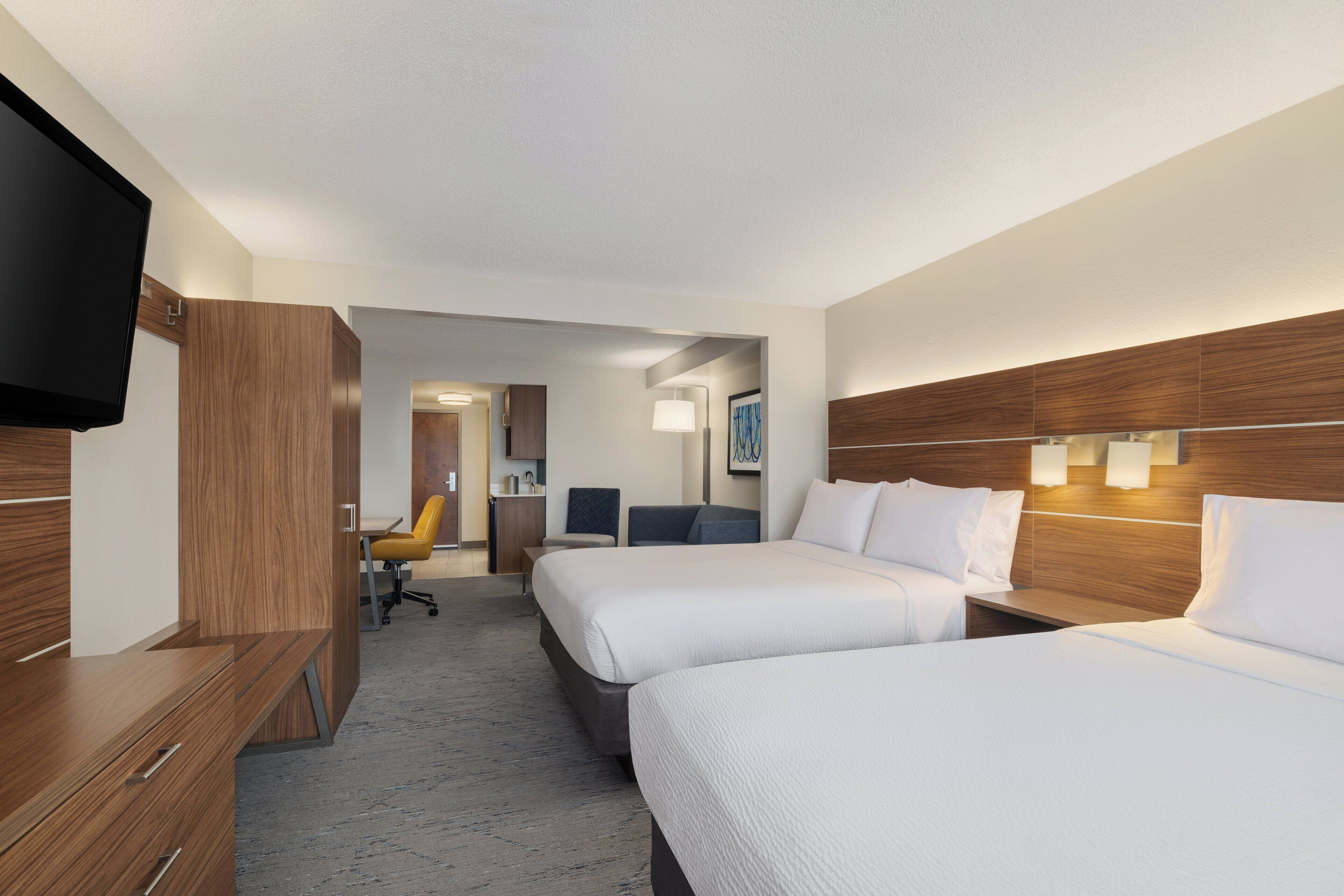 A hotel room with two beds, a desk, a TV, and a bathroom visible in the background.