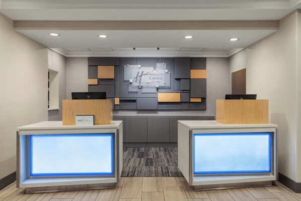 A reception area with a modern design, featuring a reception desk, a digital display, and a wall-mounted sign. - Holiday Inn Express & Suites Indianapolis Dtn-Conv Ctr Area by IHG (Indianapolis)