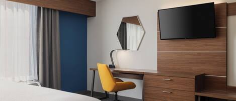 Een hotelkamer met een bed, een bureau met stoel, een flatscreen-tv en een grote spiegel.