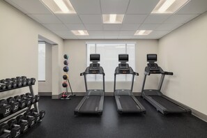 Une salle de sport équipée de tapis de course, d’haltères et d’un support à poids.
