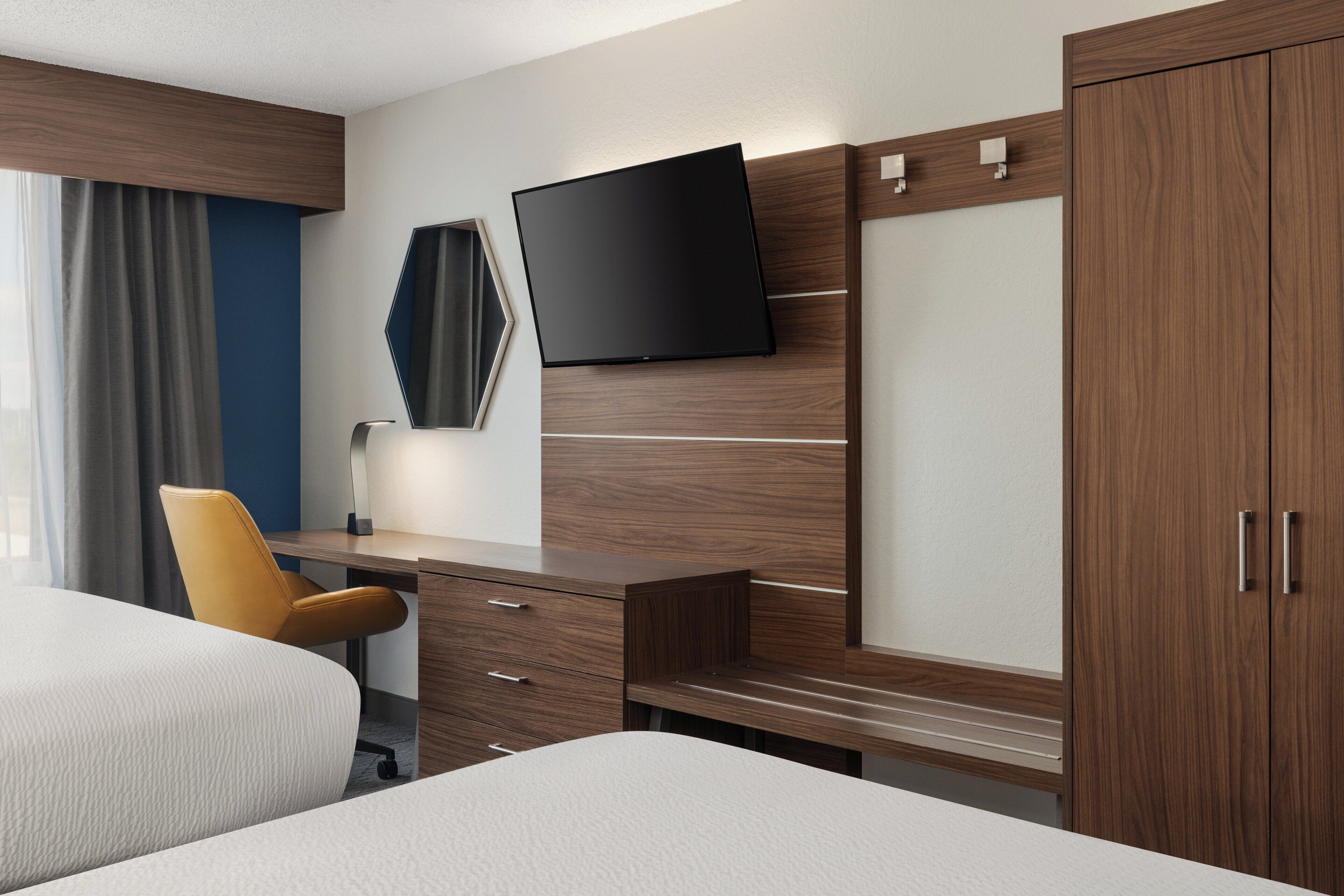 A hotel room with a bed, a desk, a chair, a TV, and a wardrobe.