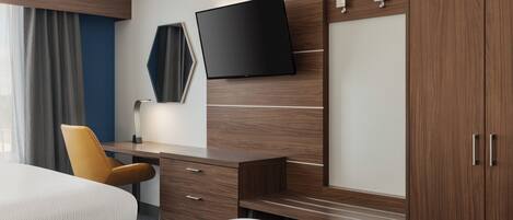A hotel room with a bed, a desk, a chair, a TV, and a wardrobe.