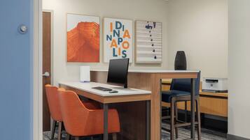 A hotel room with a desk, two chairs, a printer, and artwork on the wall.