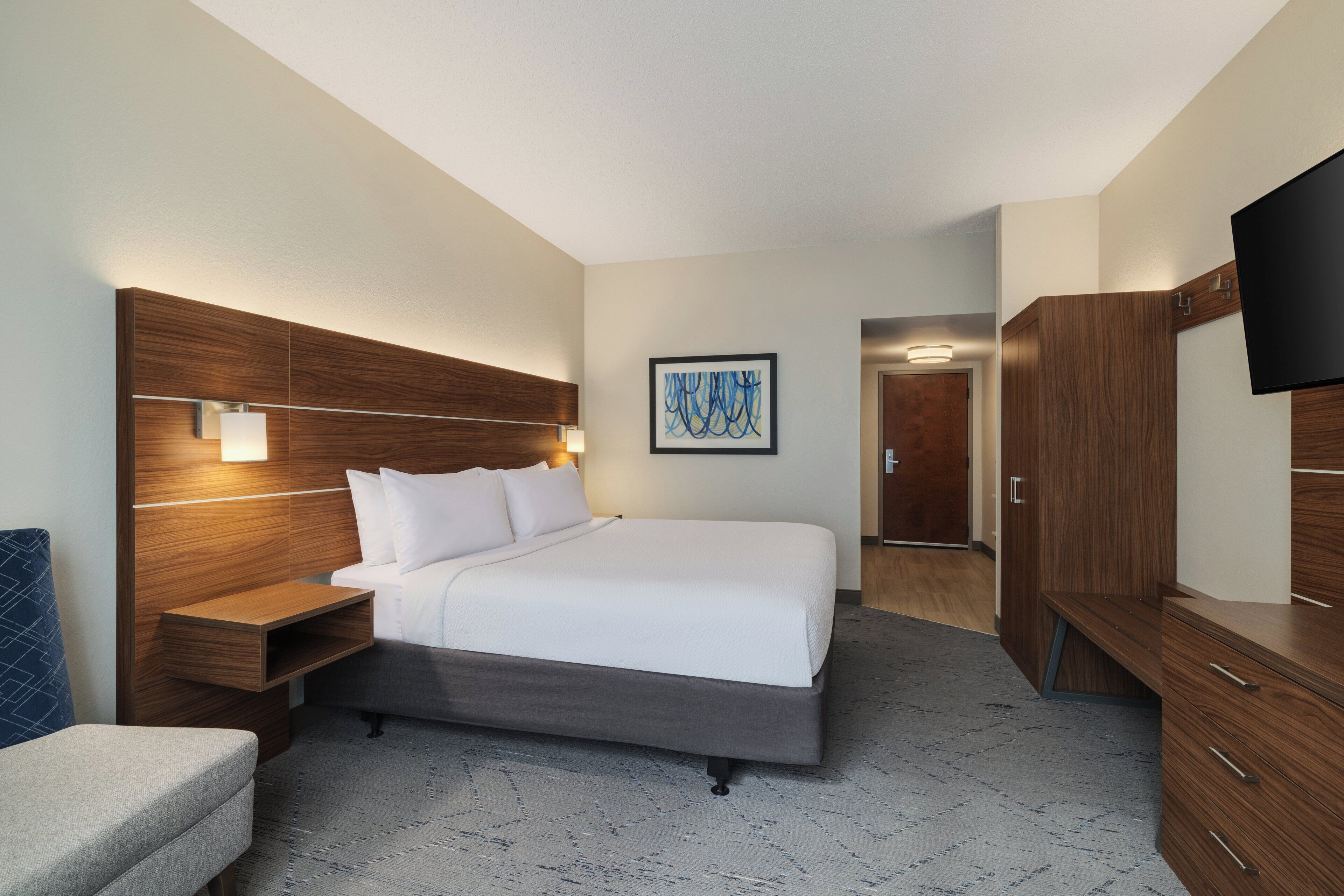 Una habitación de hotel moderna con una cama grande, mesitas de noche, un televisor de pantalla plana y un armario de madera.