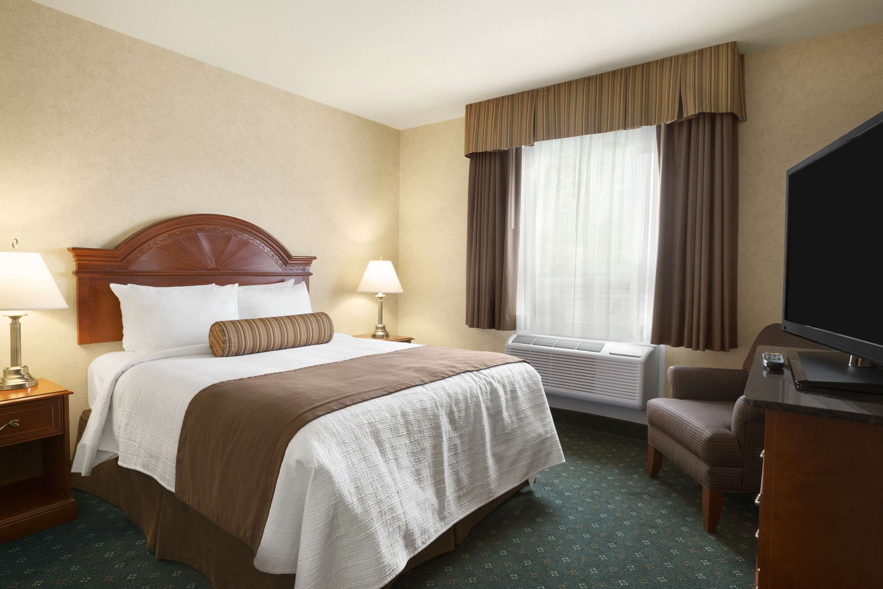Une chambre d’hôtel avec un grand lit, deux tables de chevet avec des lampes, un bureau avec une télévision et une fenêtre avec des rideaux.
