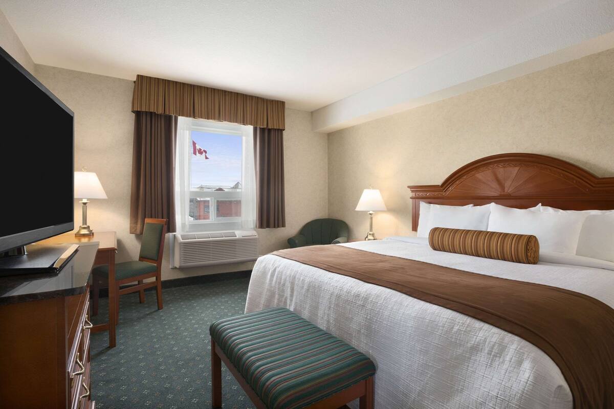 Habitación de hotel con cama, televisor, escritorio, silla, banco y ventana con cortinas.