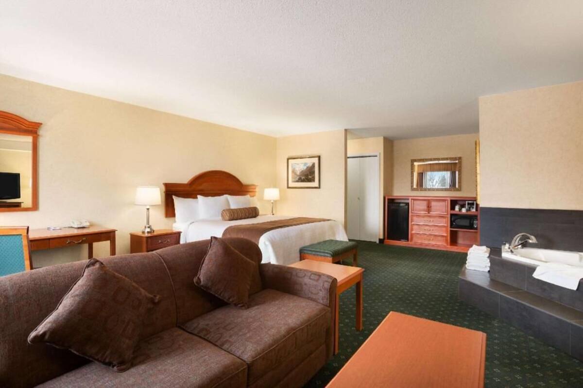 Habitación de hotel con cama, sofá, escritorio, cómoda, espejo y baño.