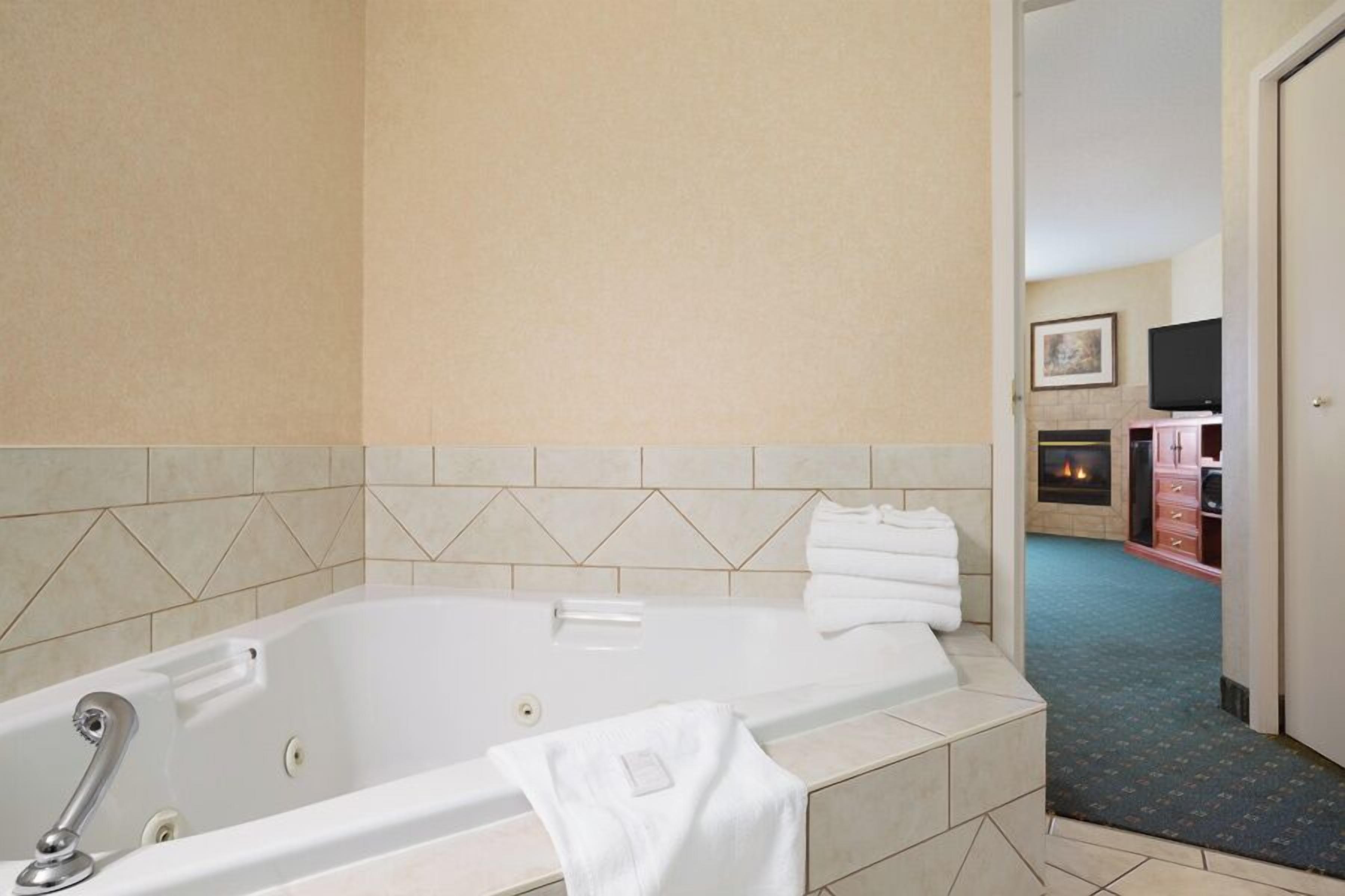 A hotel bathroom with a bathtub, a towel rack, and a visible fireplace in the background.