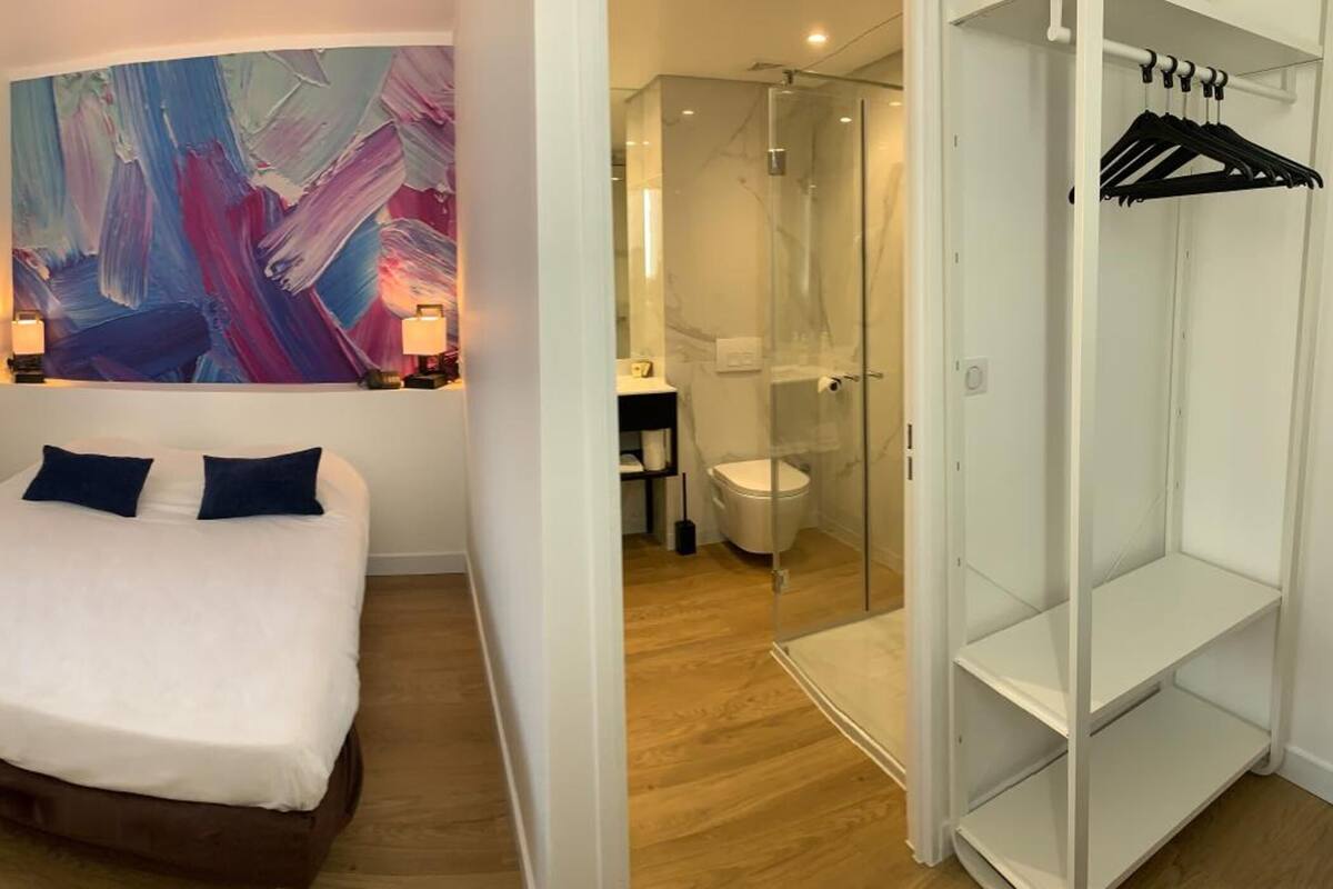 Un dormitorio con una cama grande, un cuadro en la pared, un vestidor y un baño con ducha de vidrio.