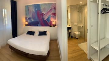 A bedroom with a large bed, a painting on the wall, a walk-in closet, and a bathroom with a glass shower.