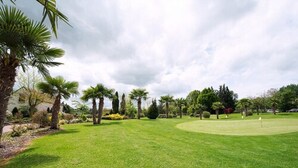 Un campo de golf bien cuidado con un putting green, rodeado de diferentes árboles y arbustos.