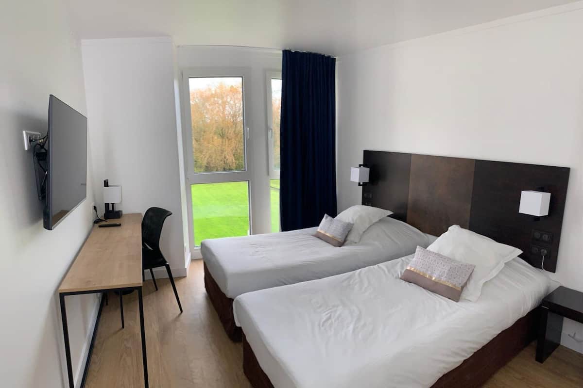 Habitación de hotel con dos camas, un escritorio, televisión y vistas al exterior.