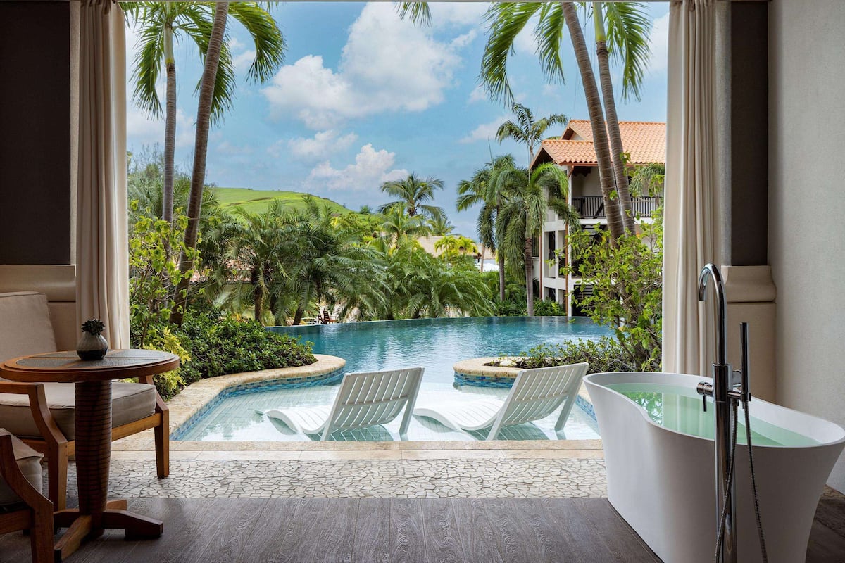 A room with a view of a swimming pool, a bathtub, and a chair.