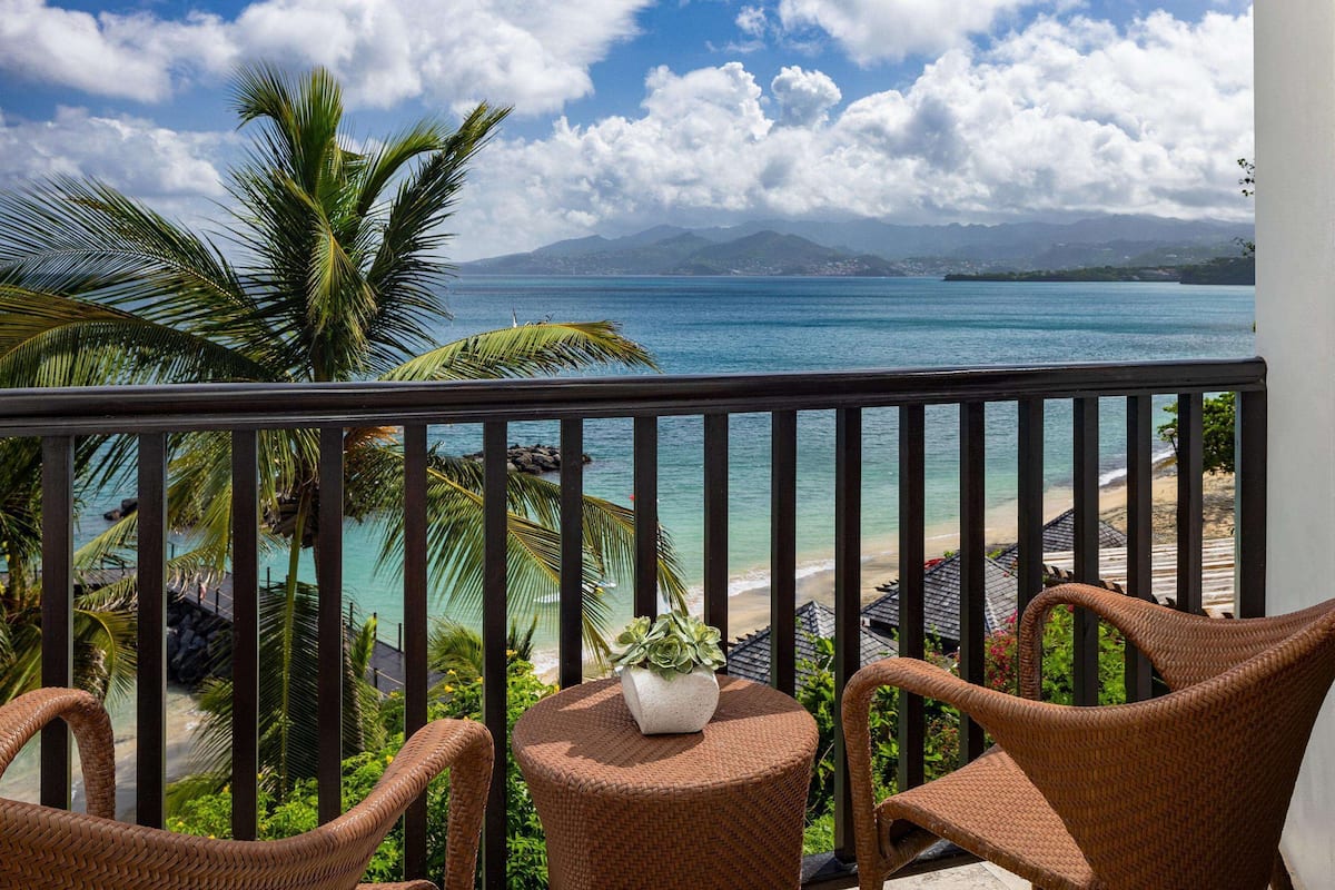 A balcony with wicker chairs, a small table with a plant, and a view of a beach and ocean.