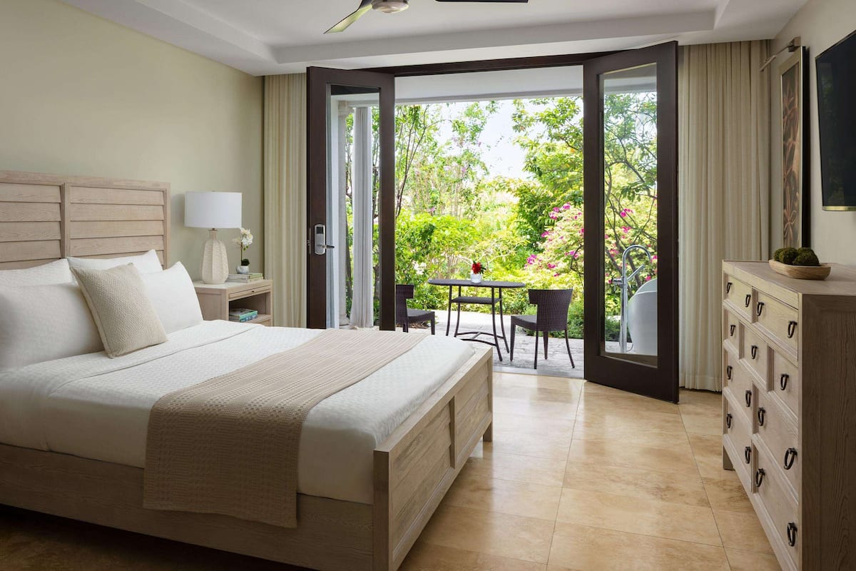 A bedroom with a large bed, bedside tables, a dresser, and a balcony with chairs and a table.