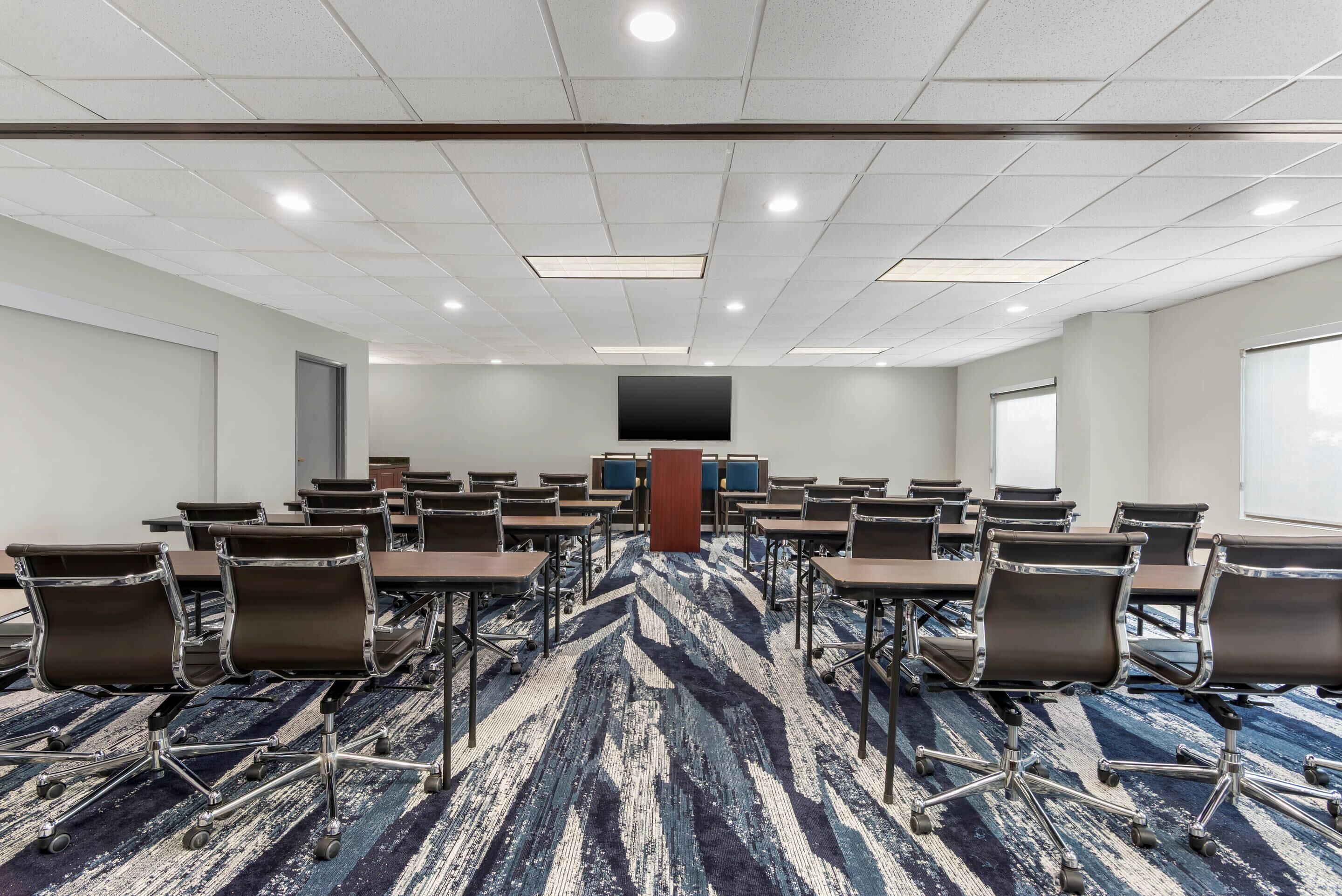 A conference room with a large screen, rows of chairs, and a patterned carpet.