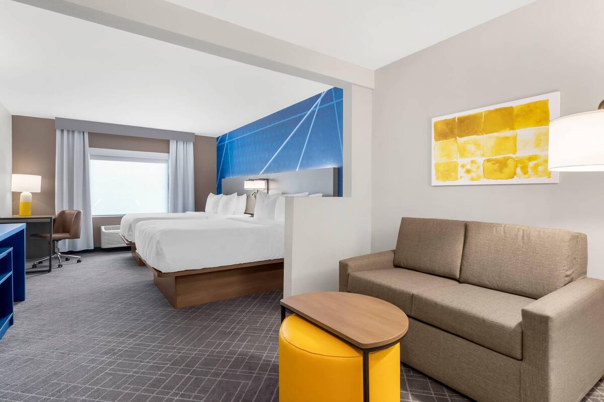 Quarto de hotel com cama, sofá, escrivaninha e uma cadeira.