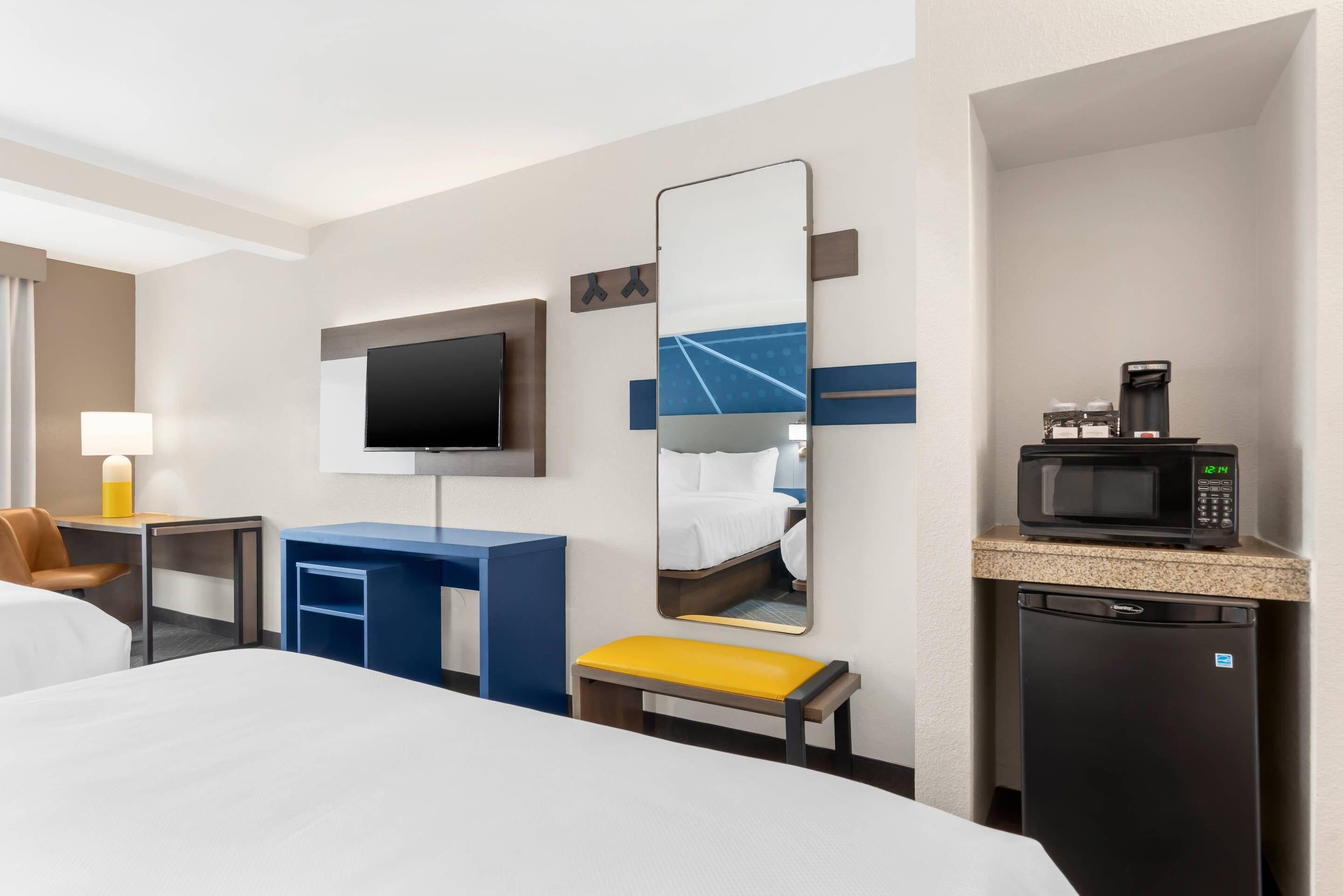 A hotel room with a bed, a desk, a chair, a television, a mirror, a microwave, and a refrigerator.