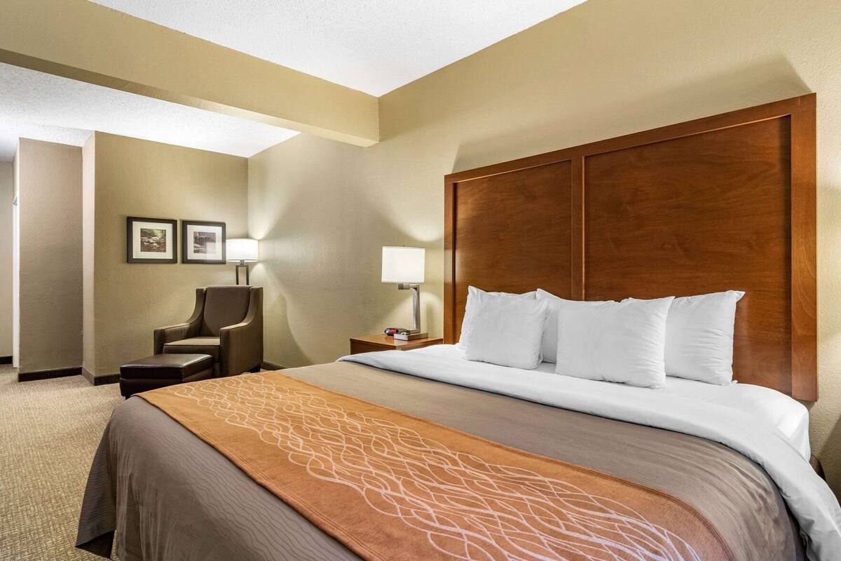 Quarto de hotel com uma cama grande, uma escrivaninha, uma cadeira e uma mesinha de cabeceira.
