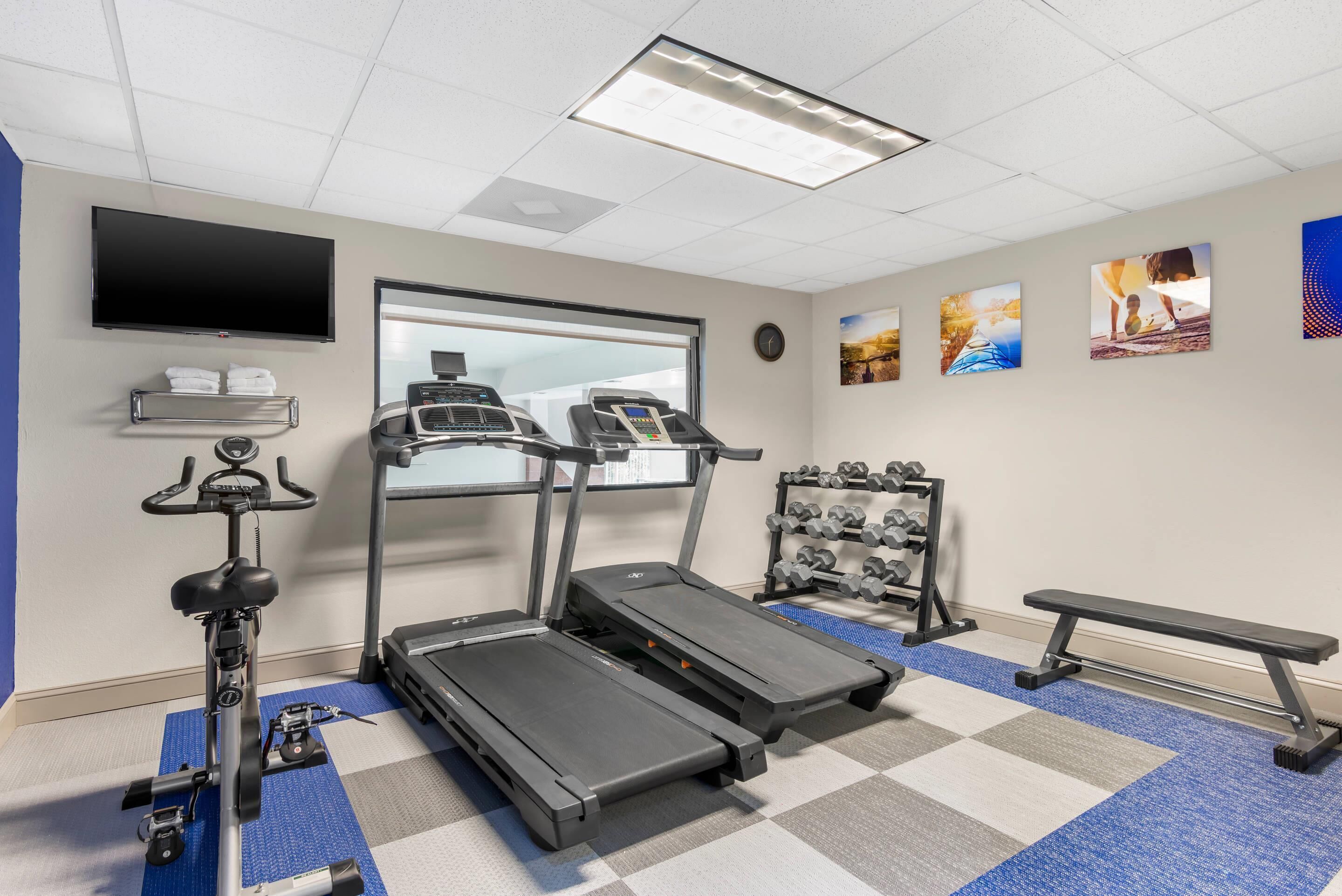 A fitness room with treadmills, a stationary bike, a bench, and a TV on the wall.