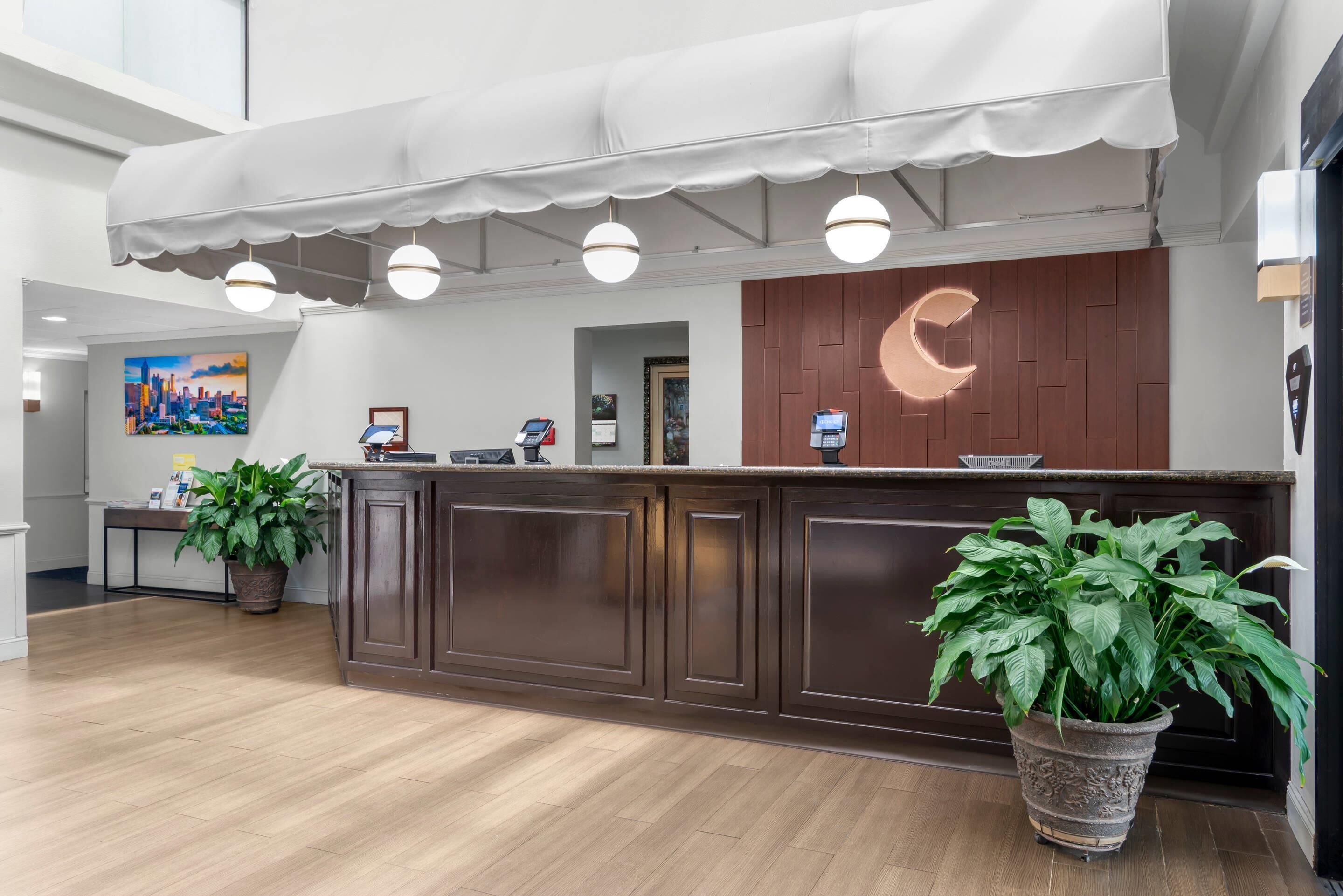 Un área de recepción con mostrador de madera, plantas en macetas, un cuadro con vista urbana y un diseño de luna creciente en la pared.