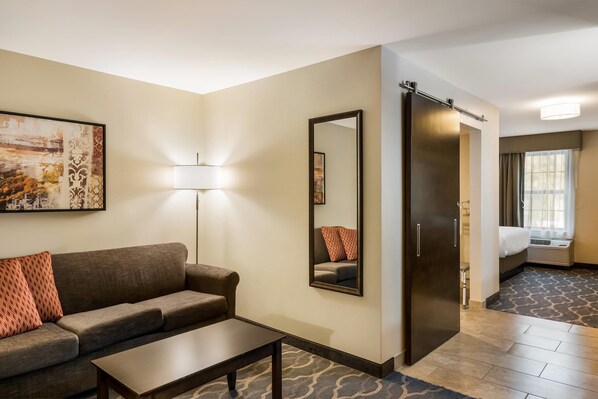 A hotel room with a sofa, a coffee table, a lamp, a mirror, and a bed with a window.