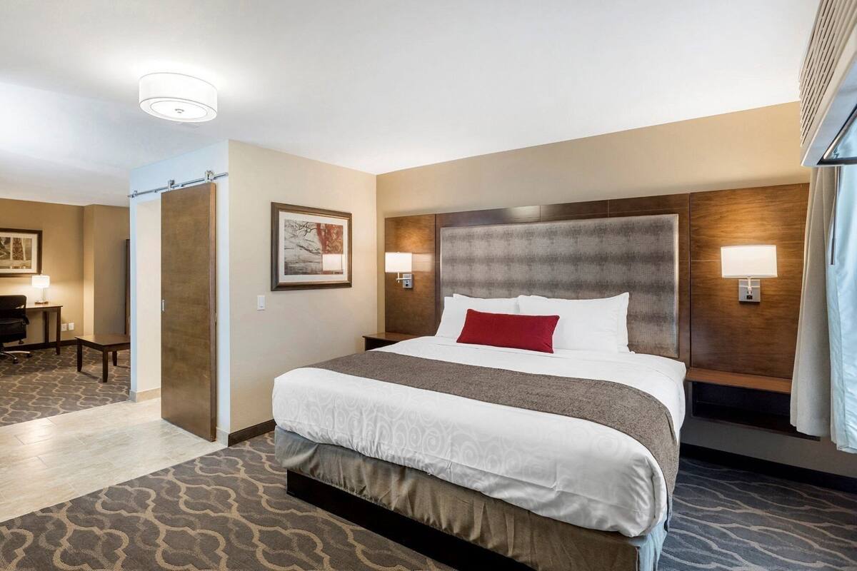 A hotel room with a large bed, a desk, a chair, a framed picture on the wall, and a window with curtains.