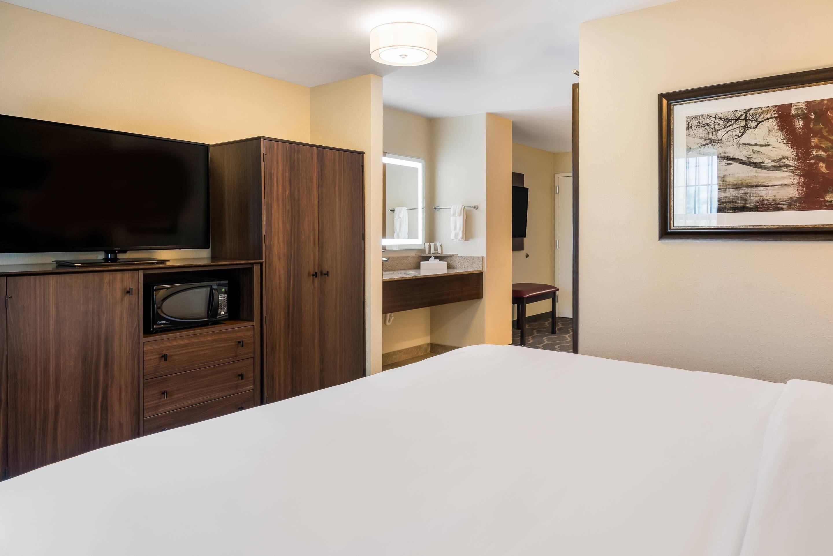 Habitación de hotel con cama, televisión, microondas, tocador con espejo y un cuadro en la pared.