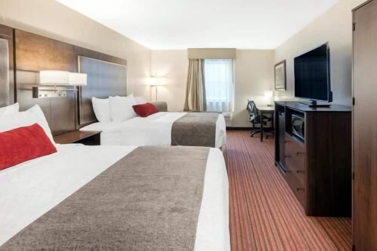A hotel room with two beds, a desk, a television, and a window with curtains.