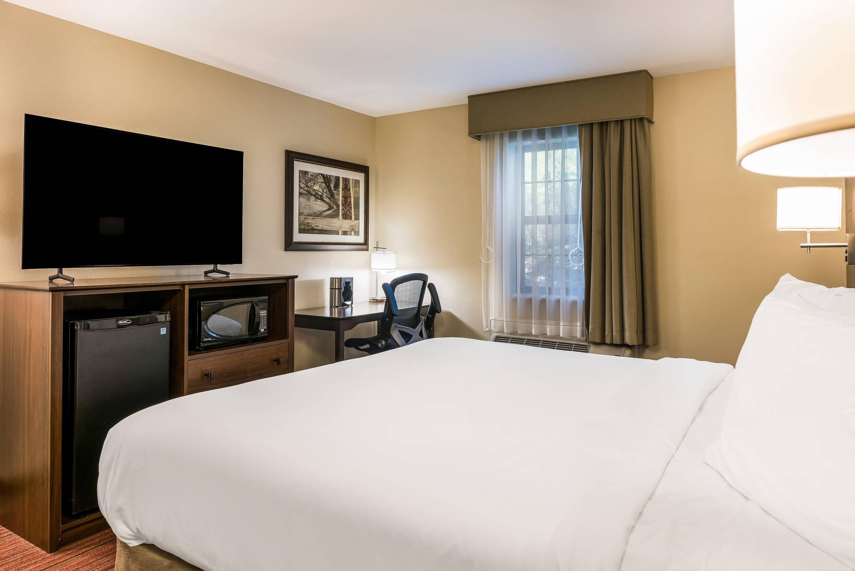 Ein Hotelzimmer mit einem großen Bett, einem Flachbildfernseher, einem Schreibtisch mit Stuhl, einer Mikrowelle und einem Kühlschrank.