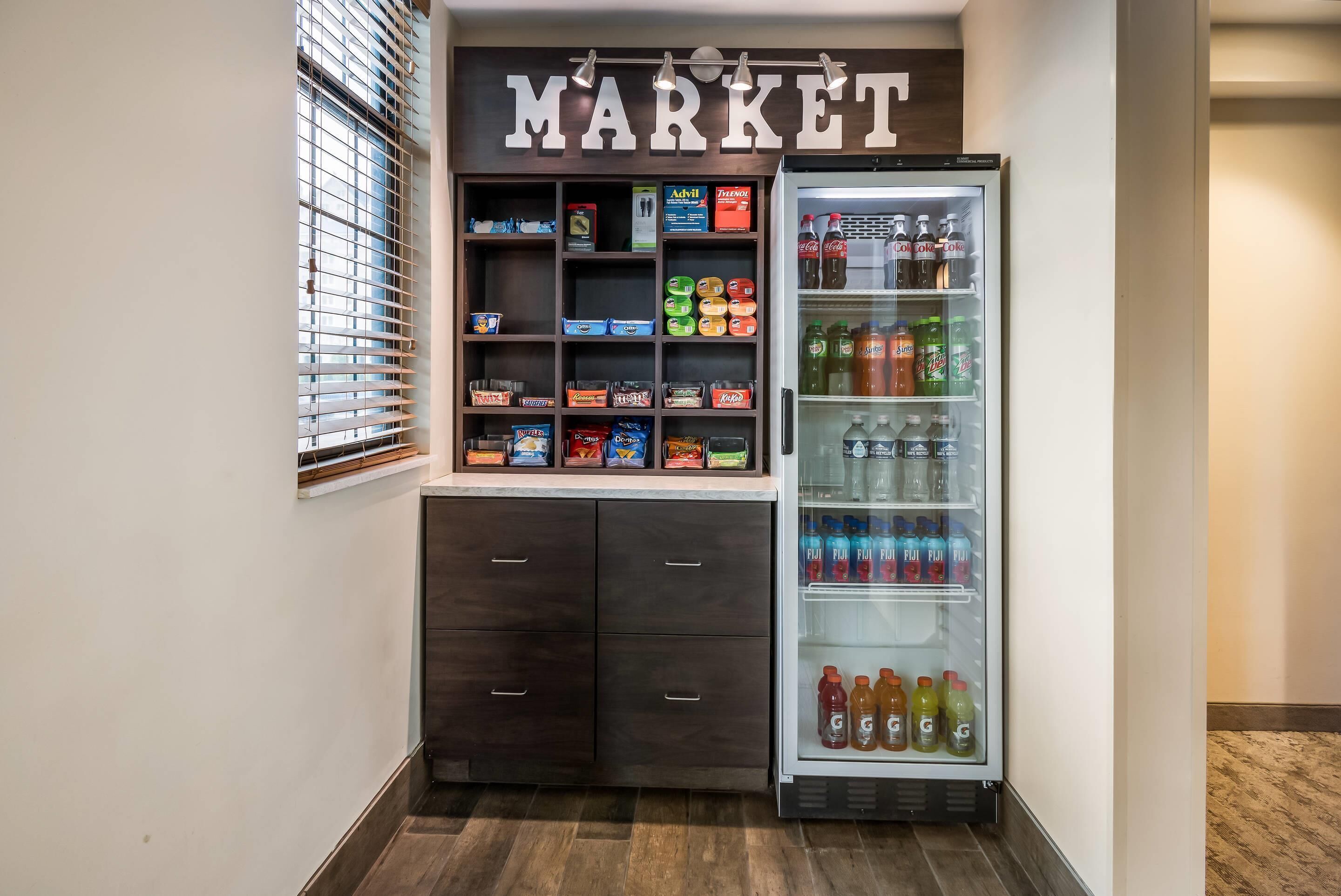 A kitchenette with a refrigerator stocked with beverages and a shelf unit with snacks and drinks.