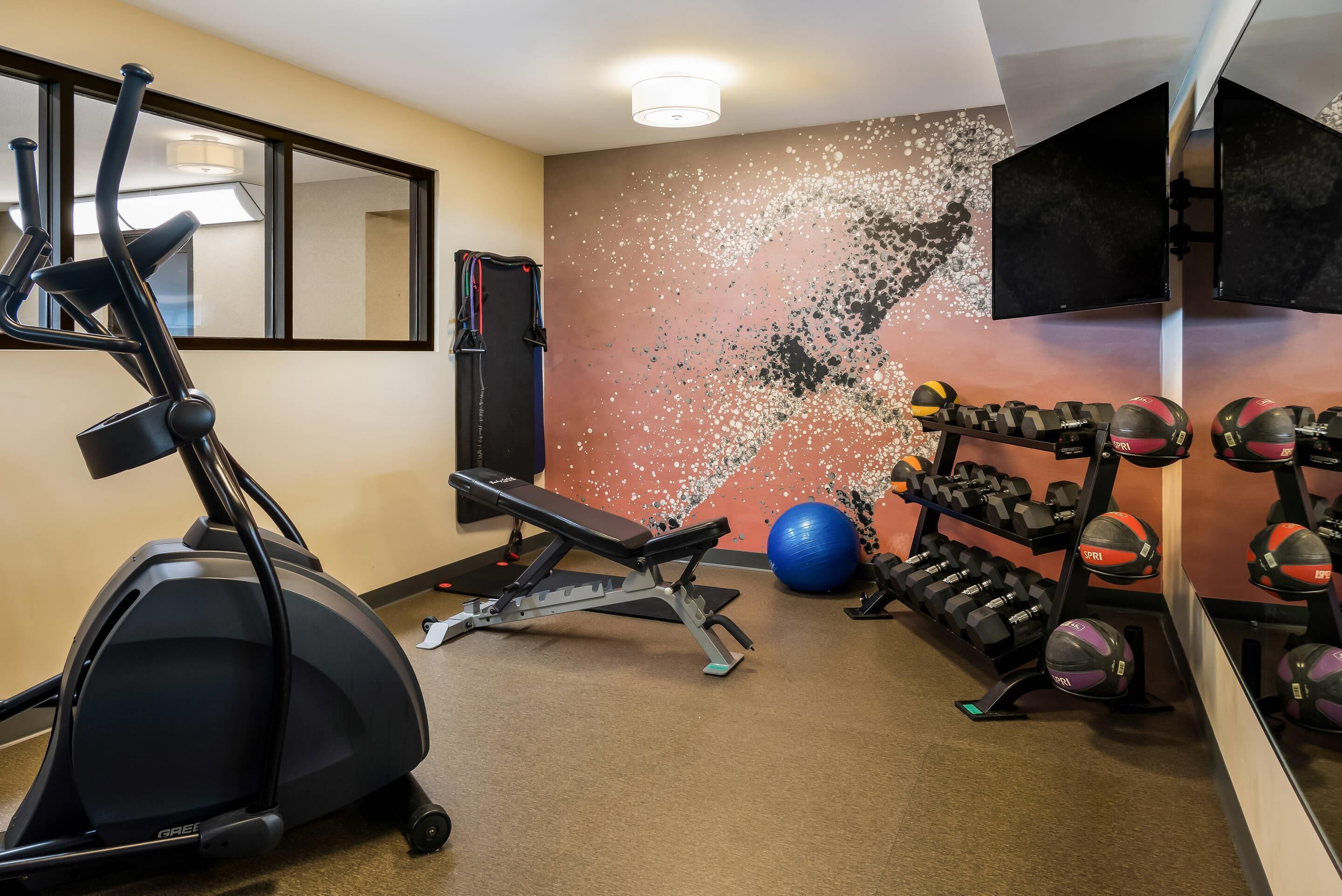 Un gimnasio con equipo de ejercicio, una pelota de ejercicios azul y un televisor montado en la pared.