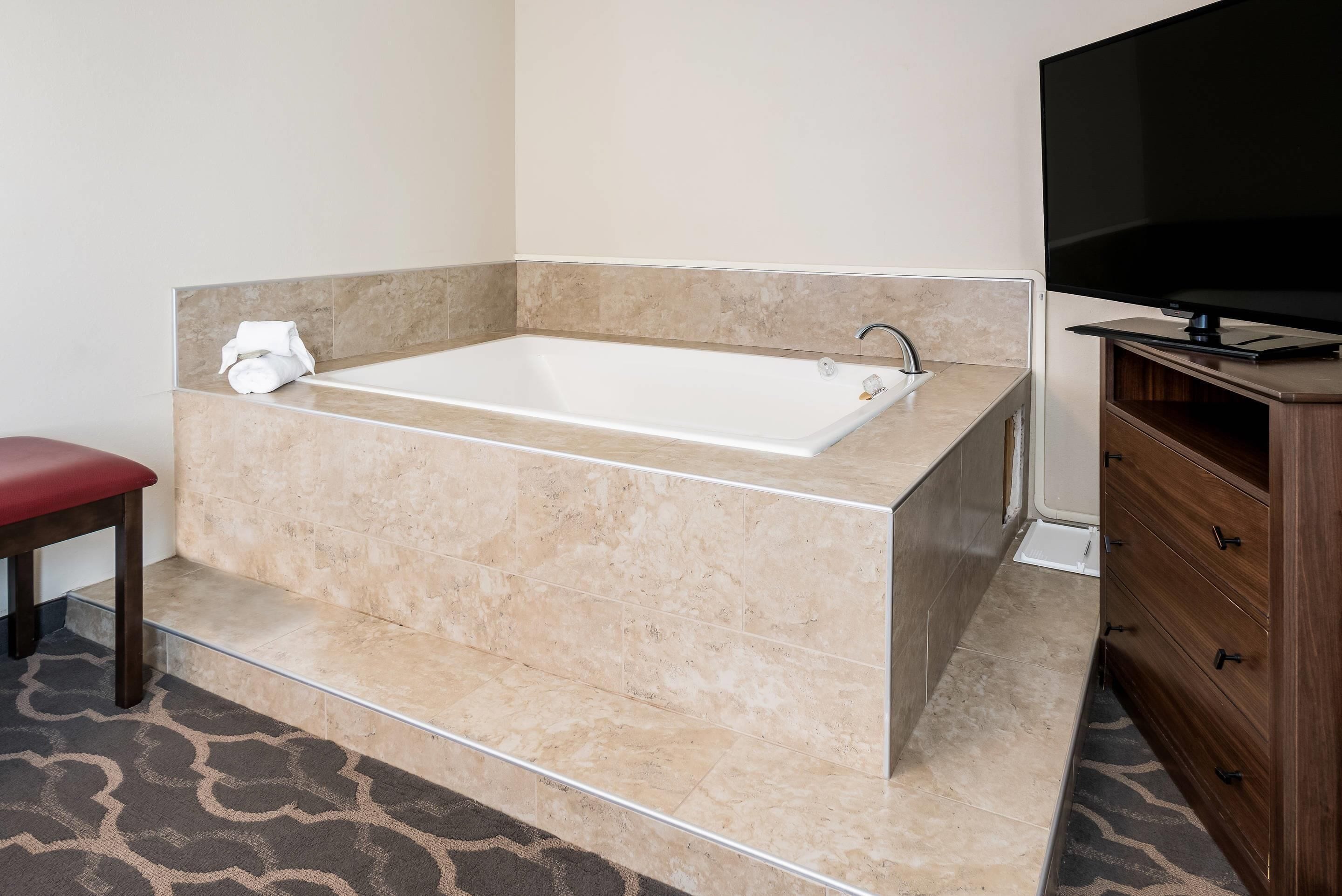 A bathroom with a large bathtub, a wooden vanity with drawers, and a red chair.