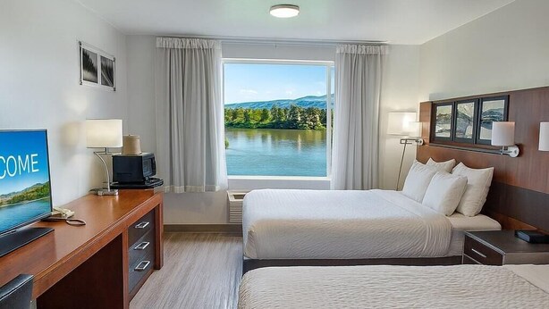 A hotel room with two beds, a desk with a television, and a view of a lake.