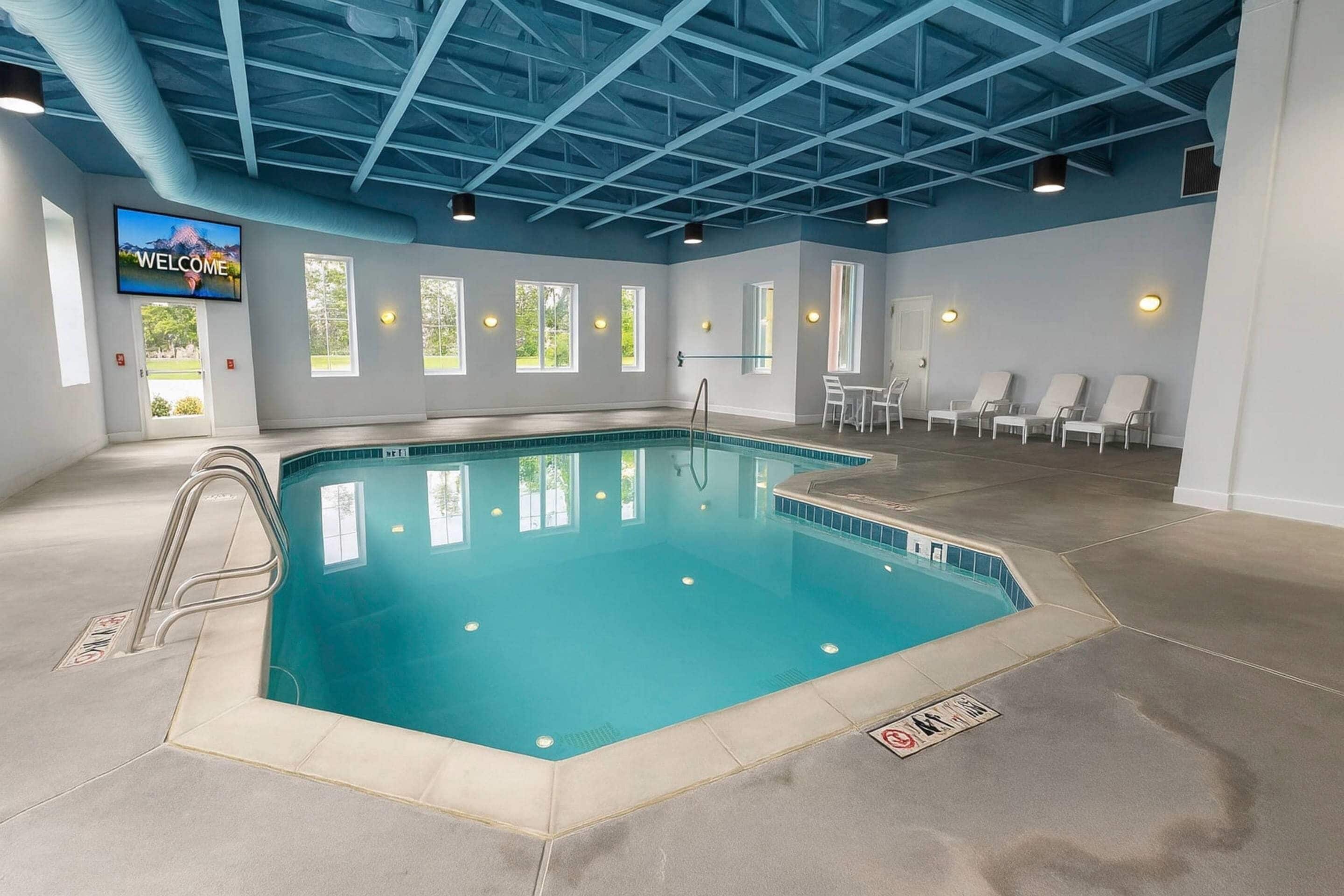 A swimming pool with a blue ceiling, a welcome screen, and lounge chairs.