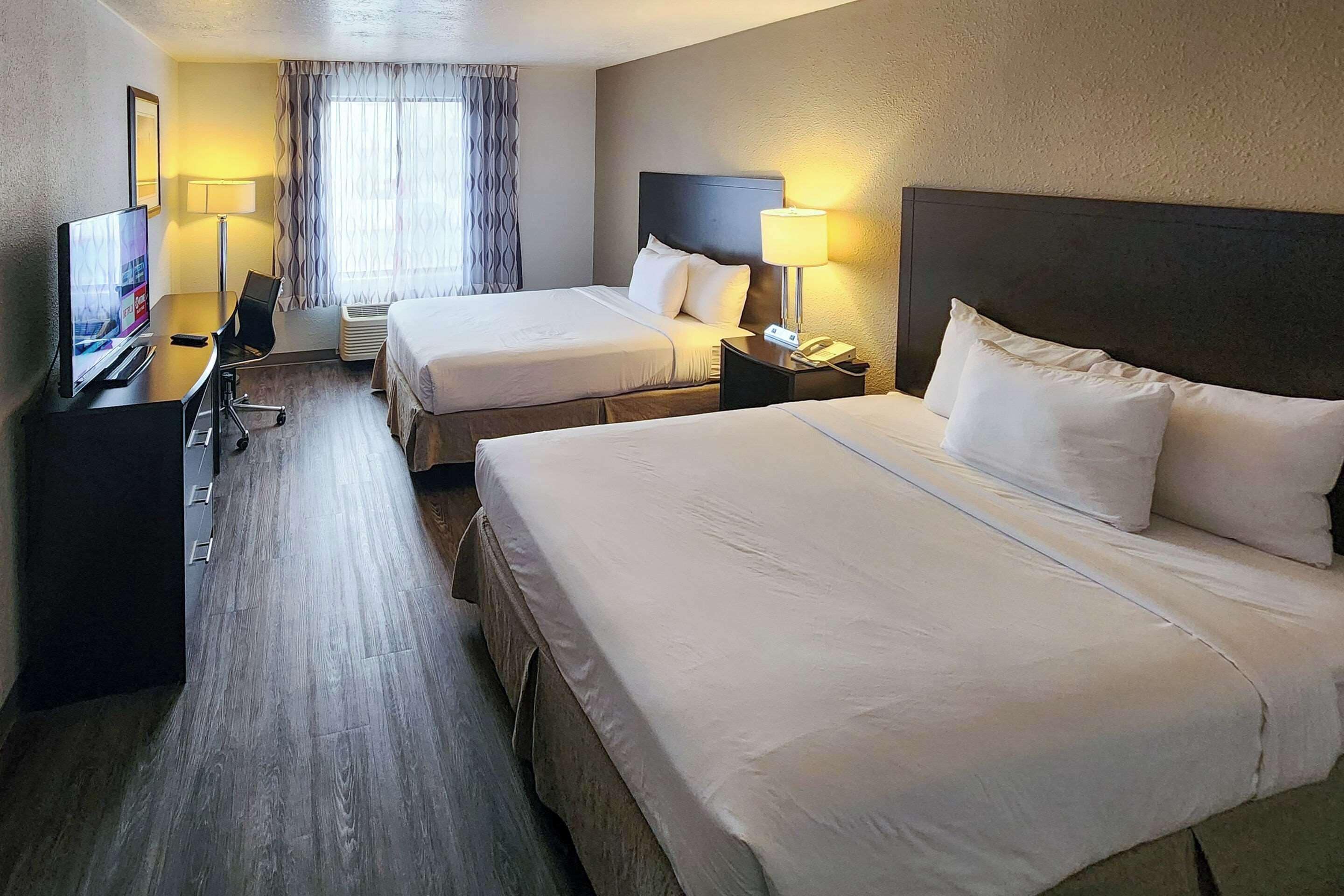 Ett hotellrum med två sängar, ett skrivbord med en dator, en lampa och en tv.